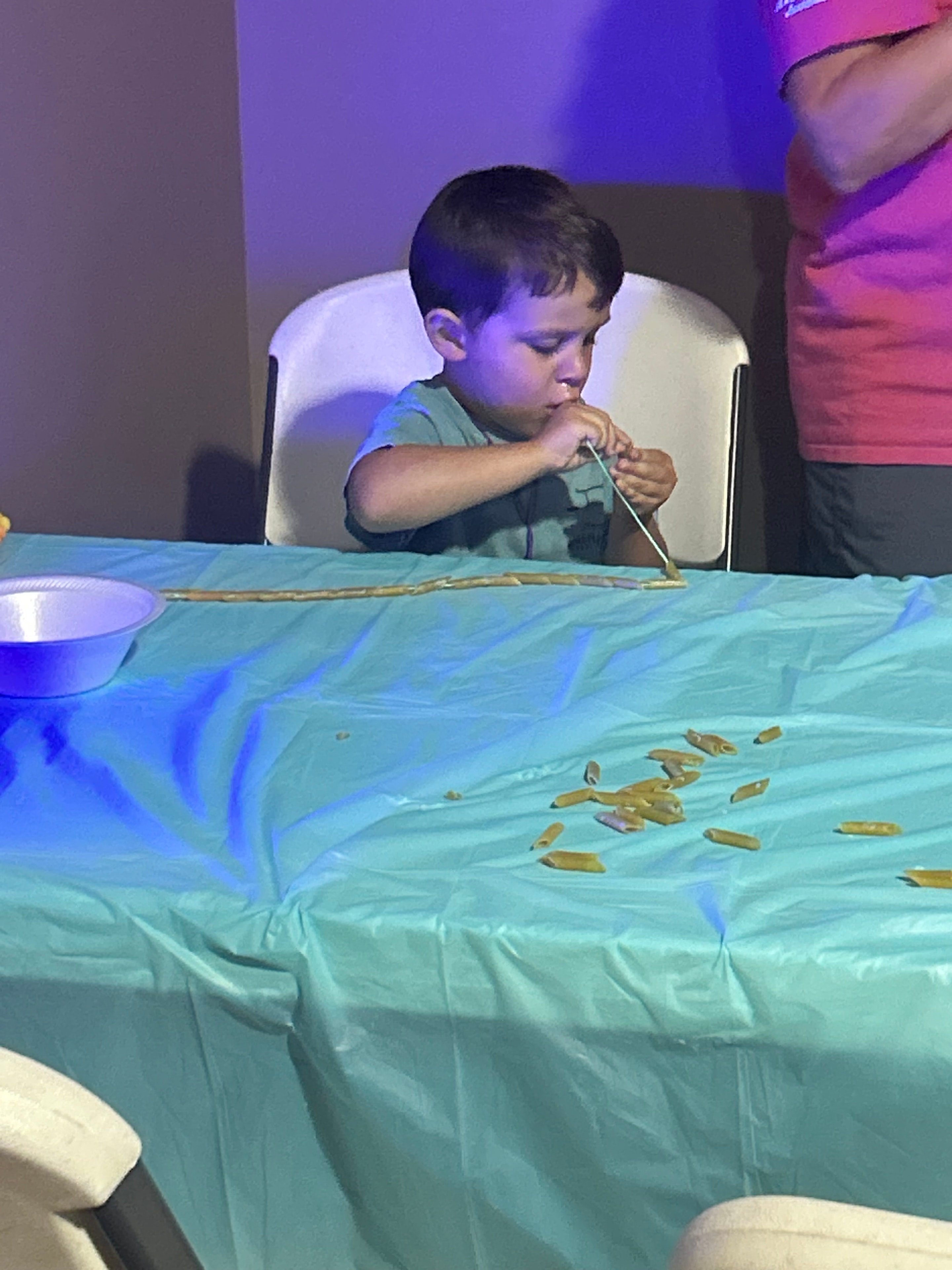 Child threading pasta onto a string during a VBS craft activity