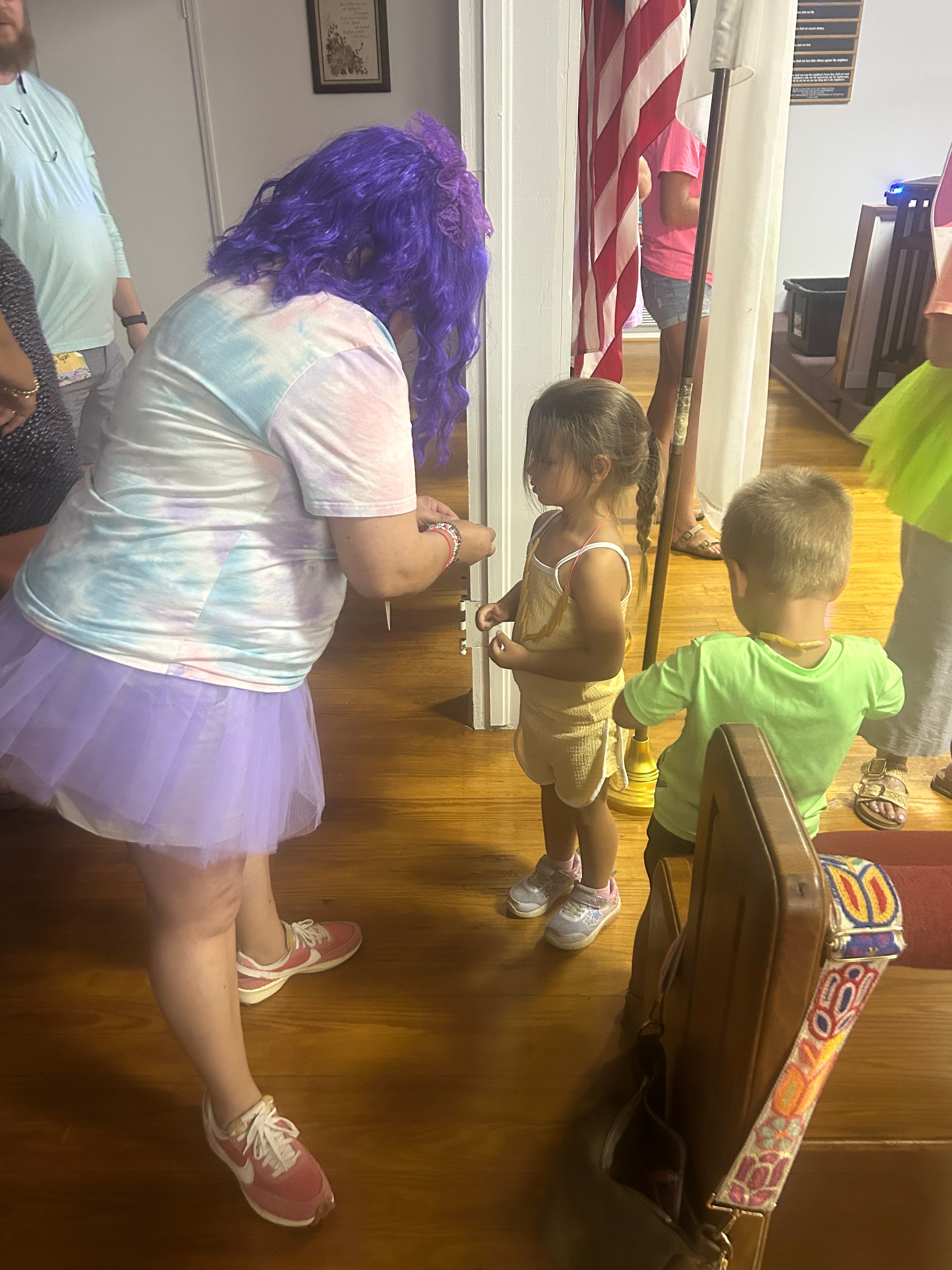 VBS volunteer in purple wig and tutu helping a child at VBS 2026