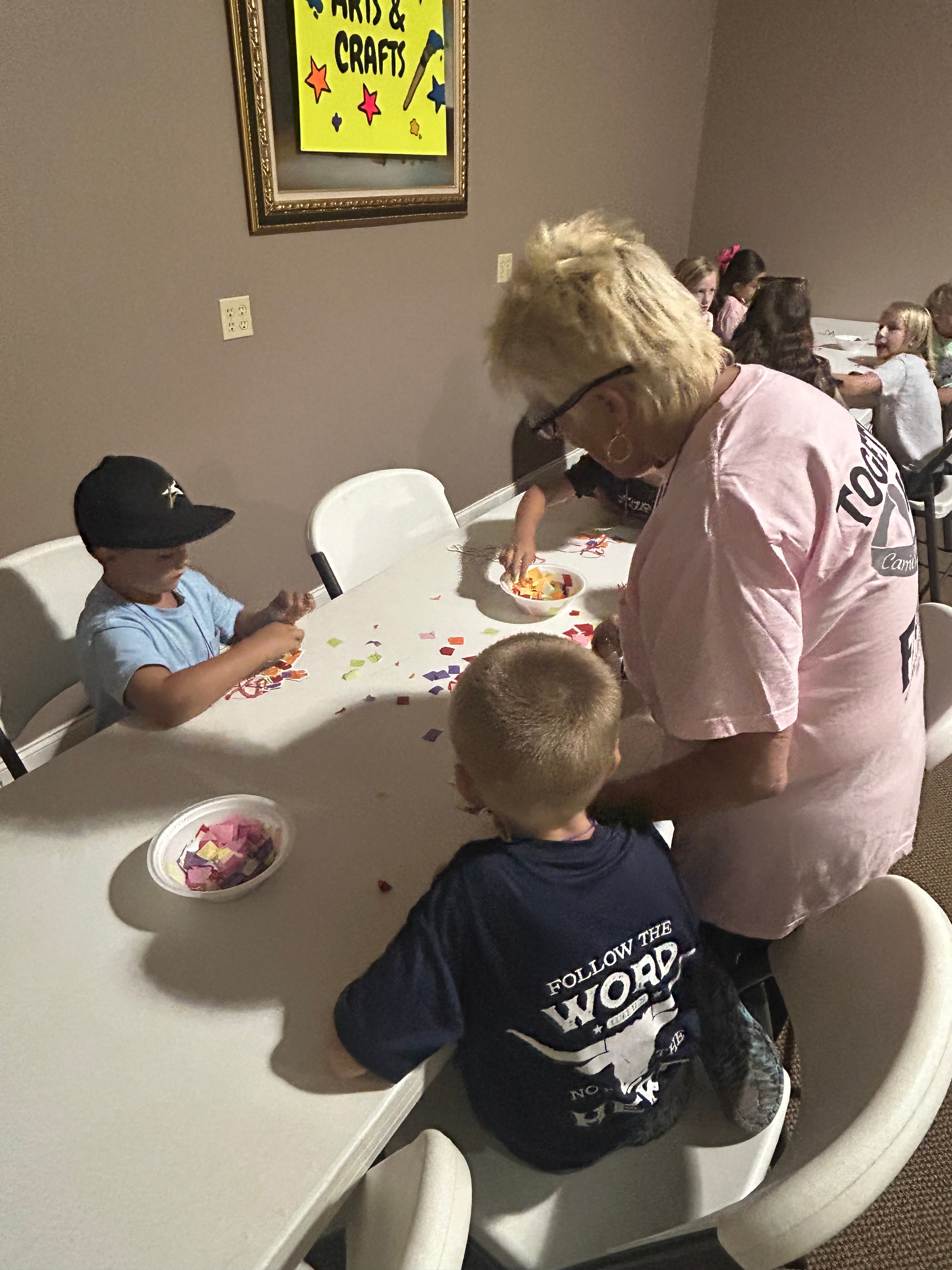 Volunteer helping children with colorful paper crafts at VBS 2026