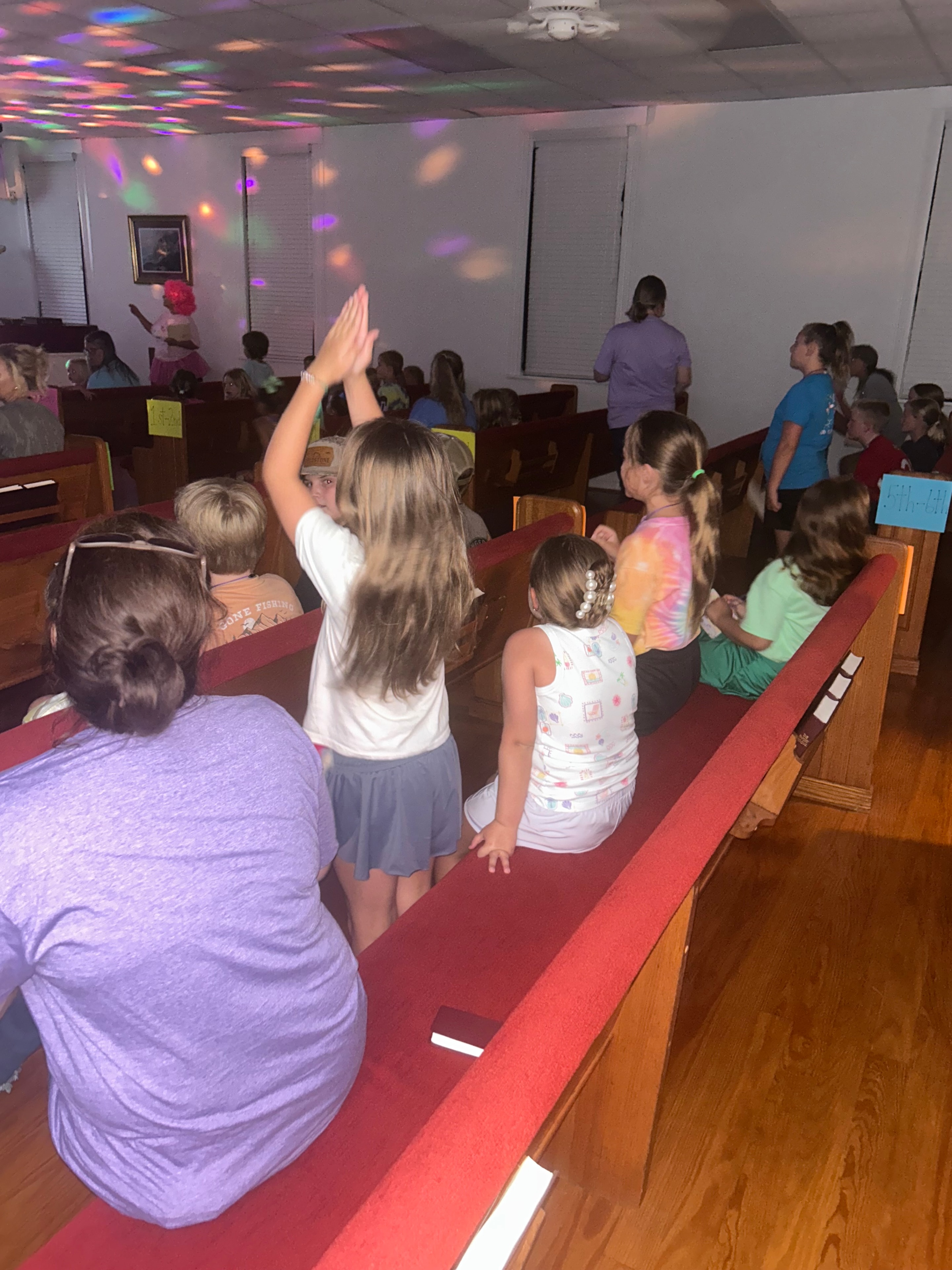 Children worshipping in the sanctuary with colorful lights during VBS 2026