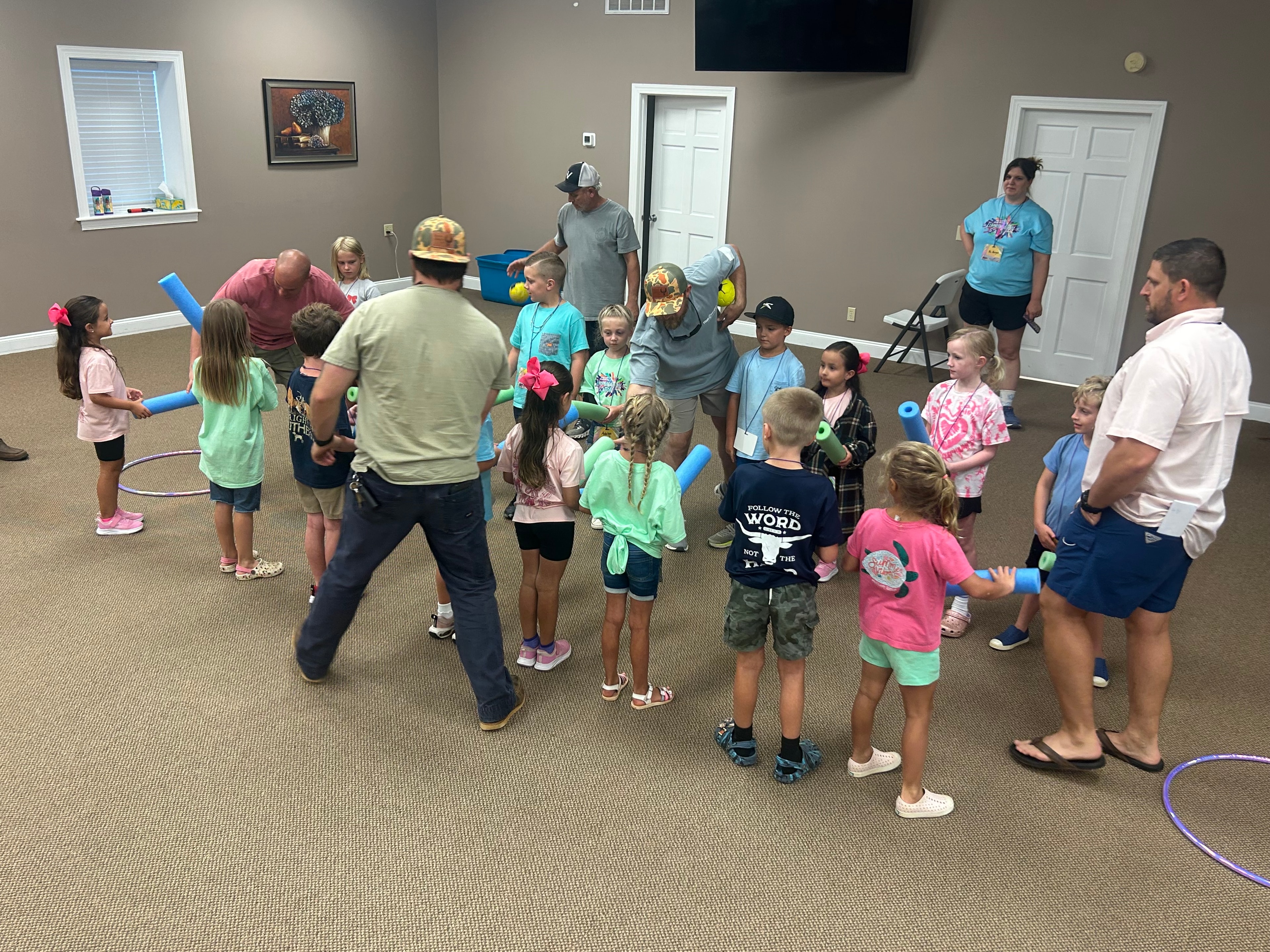 Large group of children and adults playing pool noodle and hula hoop game at VBS 2026
