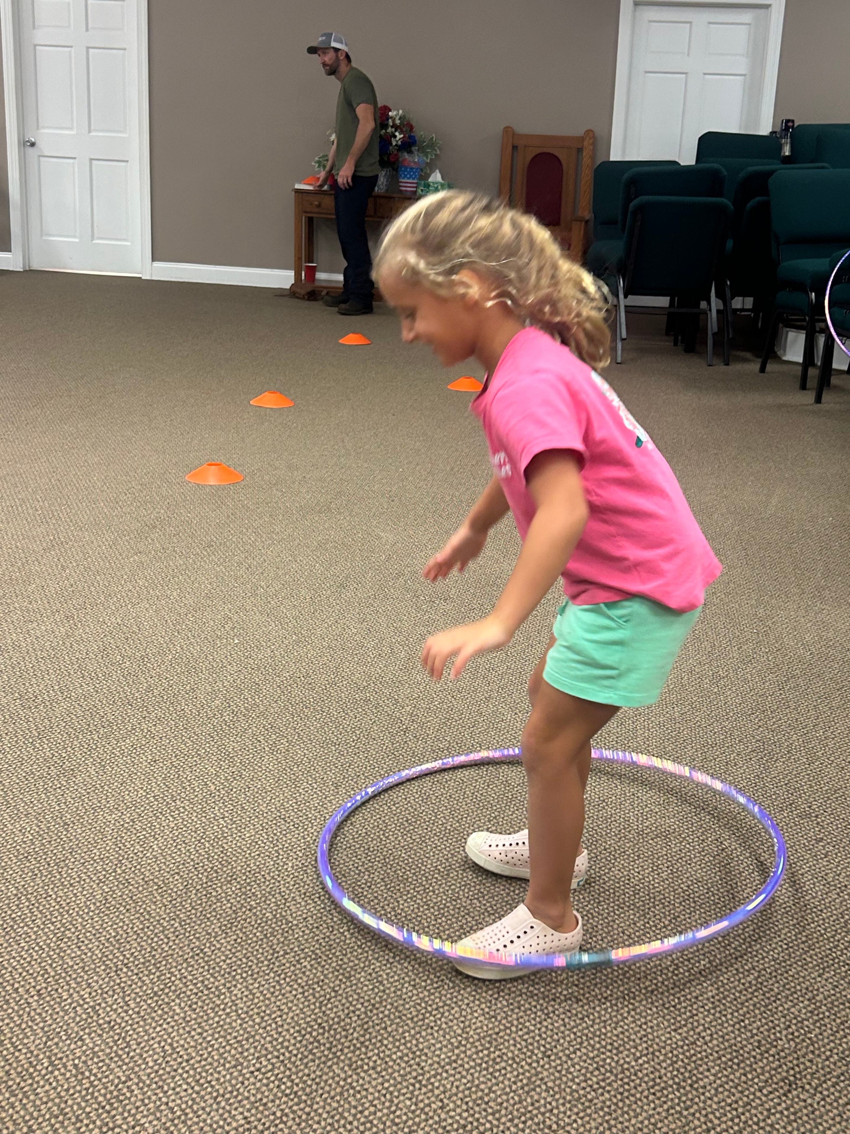 Girl in pink shirt jumping through a hula hoop over orange cones at VBS 2026